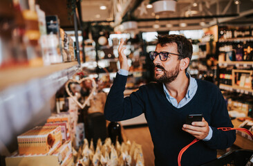 Handsome middle age man buying some healthy food and drink in modern supermarket or grocery store. Lifestyle and consumerism concept.