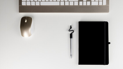 Stock photograph of a stylized white office table with a notebook and pen and blank keyboard and mouse