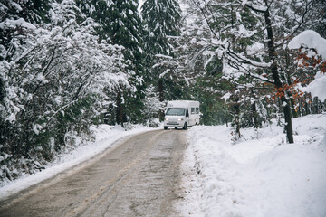 Una autocaravana en una camino de un monte nevado con arboles nevados en los costados. 