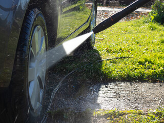 the girl washes the car at home near the garage using a pressure washer