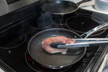 raw pork meat in a frying pan on an electric stove. searing pork chops in a frying pan