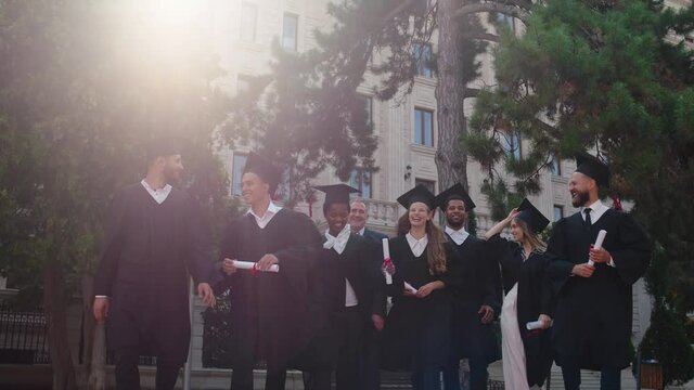 Graduation day group of multiracial graduates students in the group walking together with the college principal in front of the camera they are smiling large feeling excited throw up the graduation