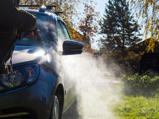 the girl washes the car at home near the garage using a pressure washer