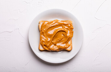 Toast with peanut butter on white ceramic plate, white concrete background, minimal concept, top view flat lay