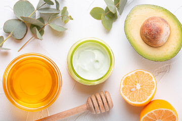 Cosmetic cream with natural organic ingredients avocado, honey, lemon and eucalyptus on white stone background, cosmetics and organic skin care for face and body care product, space for text
