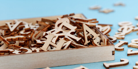 Wooden alphabet letters pile in a box on blue table. Plywood English letters background.