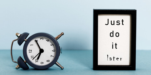 Overturned alarm clock and frame with words: just do it later. Laziness, slow life and...