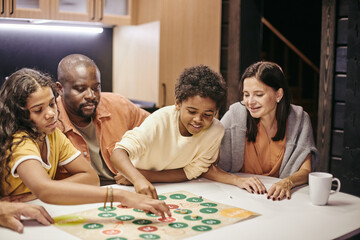 Happy parents sitting at the table and playing with children in board game at home