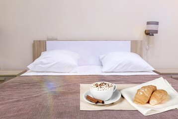 Breakfast in bed with croissant and hot coffee on tray.