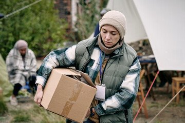 Young woman carrying box with clothes for refugees while moving along their camp