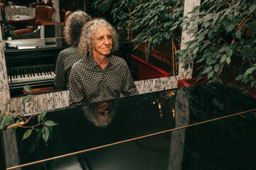 Portrait of senior man, age 60 - 65 years old, gray curly hair, sitting at piano and playing piece of music, focused, injoing melody