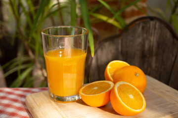 A glass of natural orange juice and fresh oranges are on the table in the summer garden. A breakfast in the garden.  Retro style image.