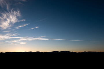 Landscape at sunset with silhouette of mountains. The plane trail crosses the sky