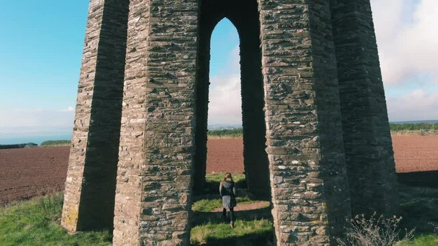 A female hiker walking through the stone arch of The Daymark Tower, in Kingswear, Devon, UK