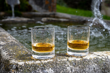 Glasses of strong scotch single malt whisky served on old stone reservoir for water from mountain spring