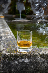 Glass of strong scotch single malt whisky served on old stone reservoir for water from mountain spring
