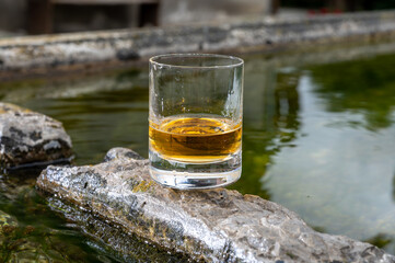 Glass of strong scotch single malt whisky served on old stone reservoir for water from mountain spring