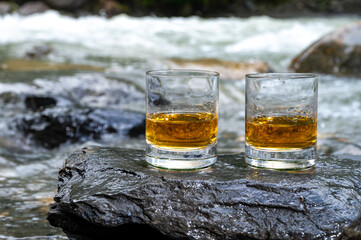 Glass of strong scotch single malt whisky with fast flowing mountain river on background