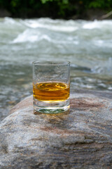 Glass of strong scotch single malt whisky with fast flowing mountain river on background