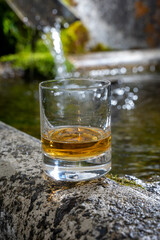 Glass of strong scotch single malt whisky served on old stone reservoir for water from mountain spring