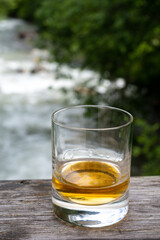 Glass of strong scotch single malt whisky with fast flowing mountain river on background