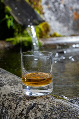 Glass of strong scotch single malt whisky served on old stone reservoir for water from mountain spring