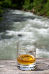 Glass of strong scotch single malt whisky with fast flowing mountain river on background