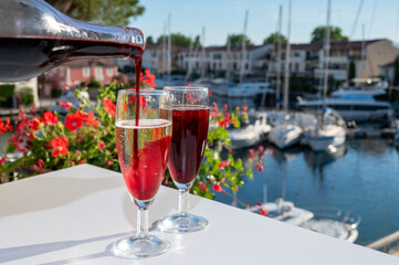Summer party with kir royal cocktail, pouring of French champagne sparkling wine and cold creme cassis in glasses in yacht harbour of Port Grimaud near Saint-Tropez, French Riviera vacation, France