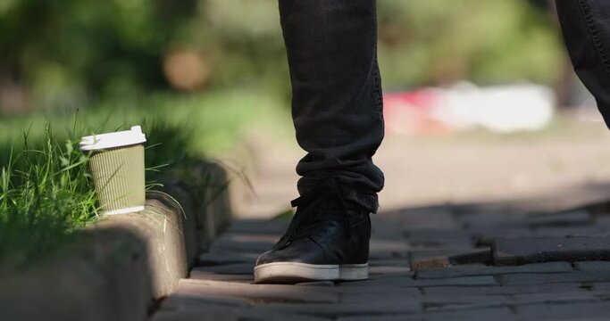 A man walks in the park, puts a paper cup of coffee on the curb of the road and leaves. People leave trash in the park while walking.