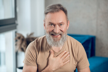 A waist up picture of a a bearded man putting hand on his heart