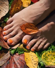 Zelfklevend Fotobehang Beautiful bare woman feet close up. Orange pedicure on the autumn background. Yellow and red fallen leaves. © berezko