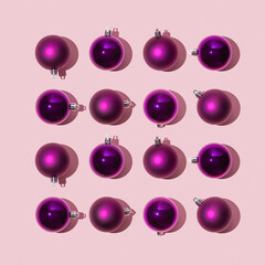 Sparkling bright christmas balls of purple color lie in the form of a square on a pink background