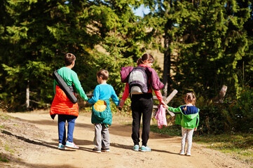Obraz premium Back of mother with three kids walking on wood mountains. Family travel and hiking with childrens.
