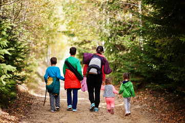 Fototapeta premium Back of mother with four kids walking on wood mountains. Family travel and hiking with childrens. Wear backpack.