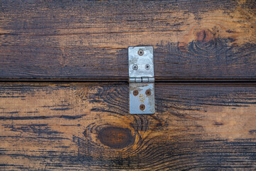 an old silver door hinge on wet varnished boards is fixed with rusty screws