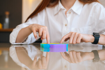 Close-up front view of unrecognizable young woman playing with rainbow pop-it fidget toy sitting at table. Closeup of female pushing colorful iridescent soft silicone bubbles sitting at desk. - obrazy, fototapety, plakaty