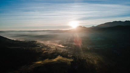 Scenic sunset at mountain range silhouette aerial view. The first or last rays of the sun. Mountains sunrise in the foggy morning above at mountain valley from drone.
