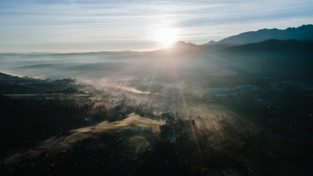 Scenic sunset at mountain range silhouette aerial view. The first or last rays of the sun. Mountains sunrise in the foggy morning above at mountain valley from drone.