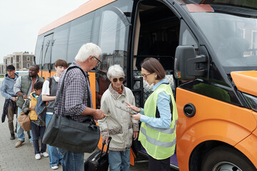 Bus conductor checking tickets of intercultural passengers standing in line along vehicle