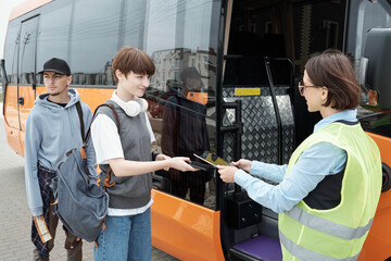 Cute teenage girl with backpack having her online ticket checked by intercity bus conductor
