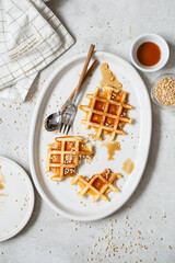 Belgian or Brussels waffles with maple syrup and puffed quinoa pops. Homemade waffles in a white oval Plate on the light gray kitchen table. Traditional classic Viennese waffles