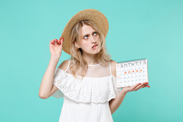 Puzzled young woman in white dress hat hold periods calendar for checking menstruation days...