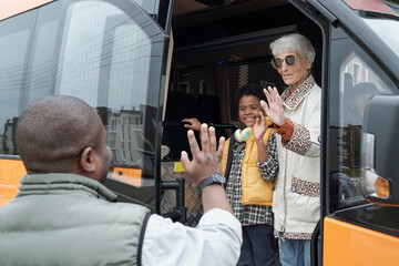Senior female and her grandson waving hands to young African man while leaving for another city