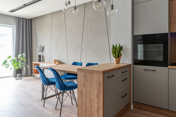 Modern interior of dininig room with stylish table with blues chairs and wooden floor. Interior of kitchen with modern lamp.