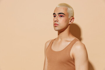 Side view young minded serious blond latin hispanic gay man 20s with make up in beige tank shirt looking aside isolated on plain light ocher background studio portrait People lgbt lifestyle concept.