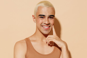 Young happy fun trendy blond latin gay man with make up in beige tank shirt hug himself look camera...