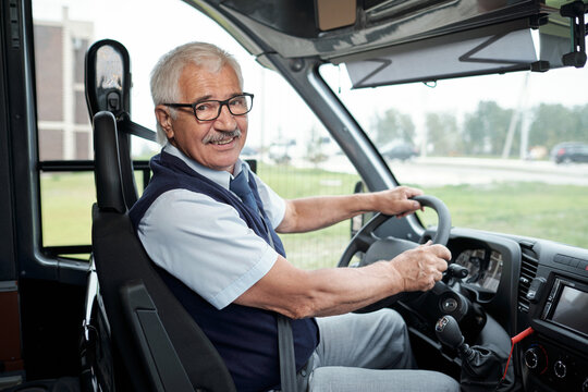 Happy aged driver of intercity bus holding by steering wheel during ride to another city or town