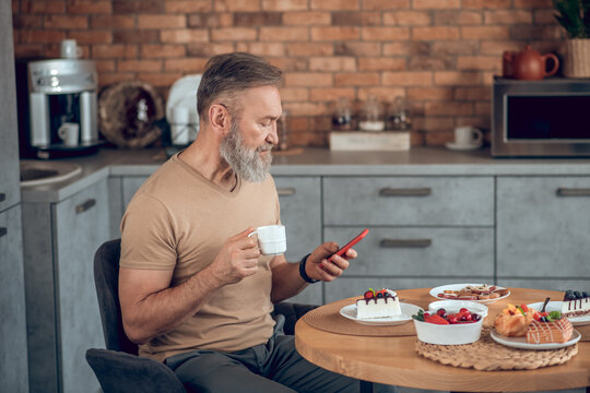 A bearded amn sitting at the table in the kitchen and looking contented