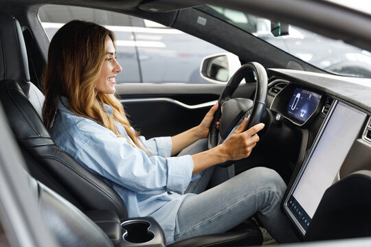 Woman customer female buyer client in blue shirt hold put hand on steering wheel choose auto want buy new automobile in car showroom vehicle salon dealership store motor show indoor. Sales concept