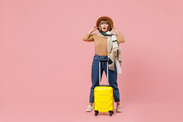 Full size body length traveler tourist shocked mature elderly senior woman 55 years old wears casual clothes hat scarf hold suitcase bag isolated on plain pastel light pink background studio portrait.